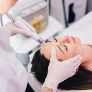Cosmetologist doing Hydradermabrasian treatment on woman face in beauty clinic